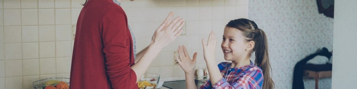 Happy young mother and cute funny daughter playing clapping hands game and have fun while cooking in kitchen at home. Family, cooking and people concept