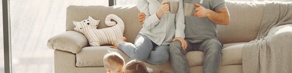 Cheerful family smiling while spending weekend together sitting parents sitting on comfortable sofa while children resting on carpet and playing